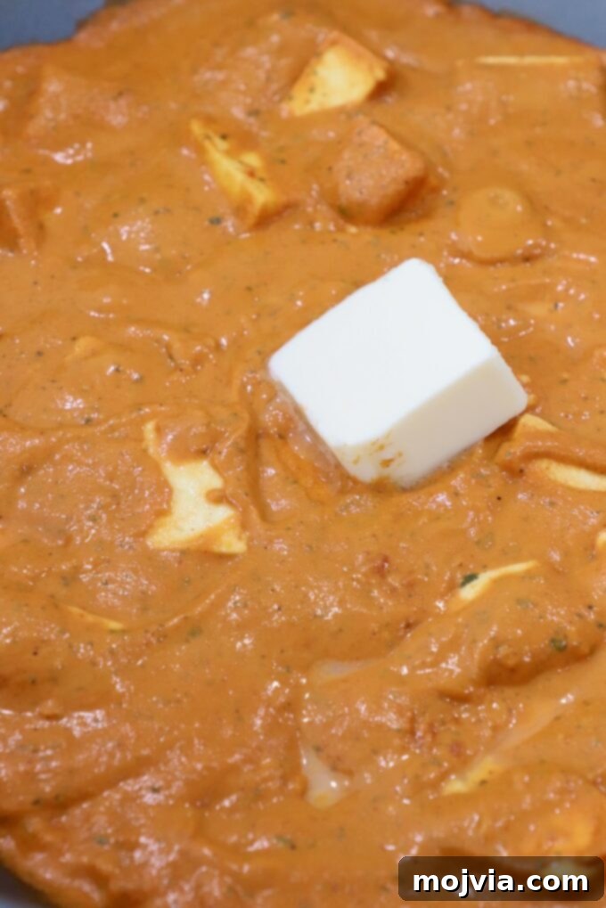 Buttery Paneer Indulgence 11 paneer in curry sauce in large pan topped with a cube of butter