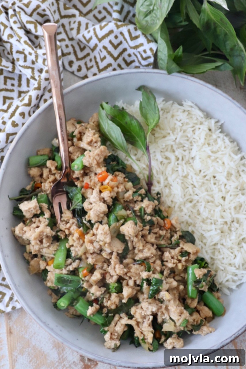 Spicy Thai Basil Chicken Stir-fry 2 Prepared Thai Basil Chicken in a bowl with cooked white rice and fresh Thai basil leaves, showcasing a vibrant and authentic street food dish.