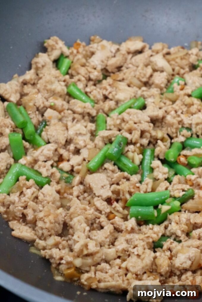 Spicy Thai Basil Chicken Stir-fry 6 Cooked ground chicken with green beans in a large pan, showing the stage before the sauce is added to the Thai Basil Chicken.