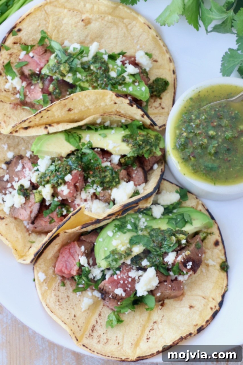 Sizzling Flank Steak Tacos 2 three tacos on plate filled with grilled steak, avocado and chimichurri sauce