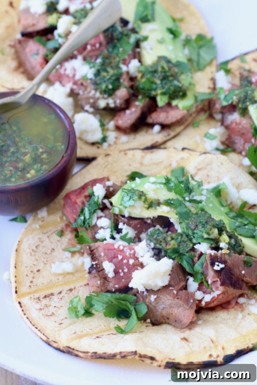 Sizzling Flank Steak Tacos 13 grilled steak in tortillas on plate topped with cotija cheese, avocado and chimichurri sauce