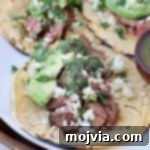 Sizzling Flank Steak Tacos 14 grilled diced steak in tacos with avocado and chimichurri sauce on white plate