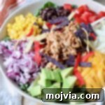 salad in bowl topped with shredded bbq chicken and vegetables