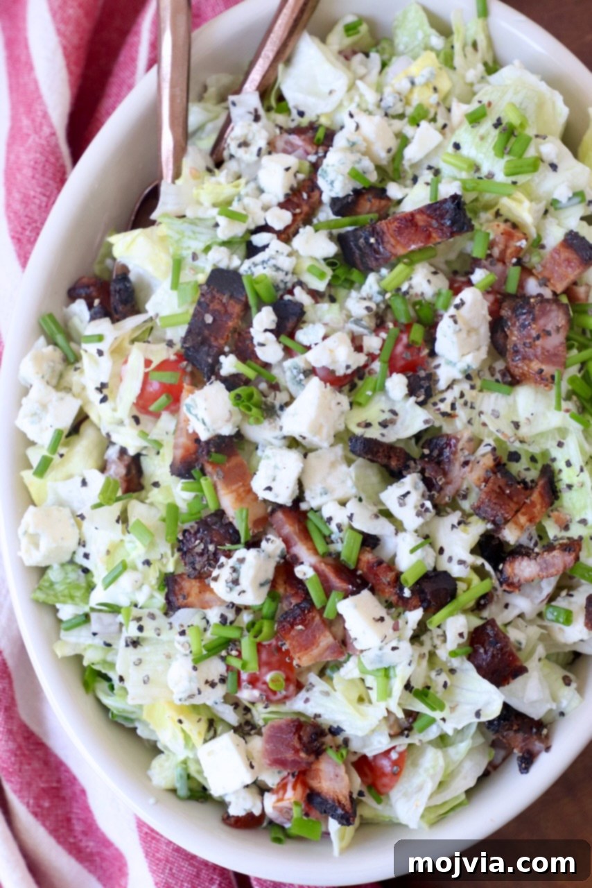 Tangy Blue Cheese Greens 4 A large bowl of chopped blue cheese salad, garnished with extra blue cheese crumbles and crispy bacon, showcasing its vibrant ingredients.