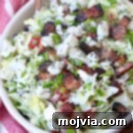 A visually appealing chopped salad in a bowl, generously topped with blue cheese crumbles and crispy bacon, ready for serving.
