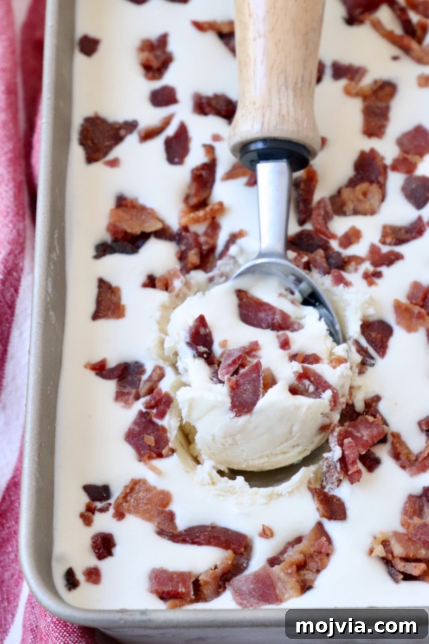Maple Bacon No-Churn Ice Cream 2 A scoop of rich Maple Bacon Ice Cream in a metal container, garnished with crispy candied bacon pieces.