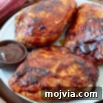 Grilled BBQ chicken breasts on a plate with a side bowl of barbecue sauce, ready for serving.