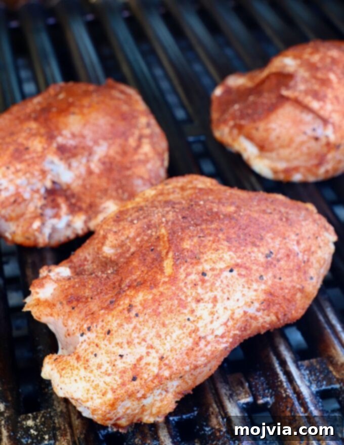Smoked Chicken Feast 7 Close-up view of seasoned chicken breasts cooking slowly on the indirect heat side of the grill, lid closed.
