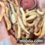 Cooked french fries in a basket with a side bowl of ketchup, ready to be served.