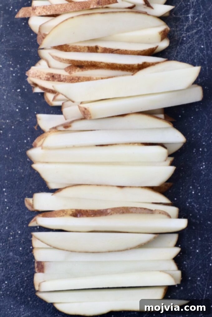 Crispy Air Fryer Fries 4 Russet potatoes expertly sliced into uniform french fries on a cutting board, ready for the next step.