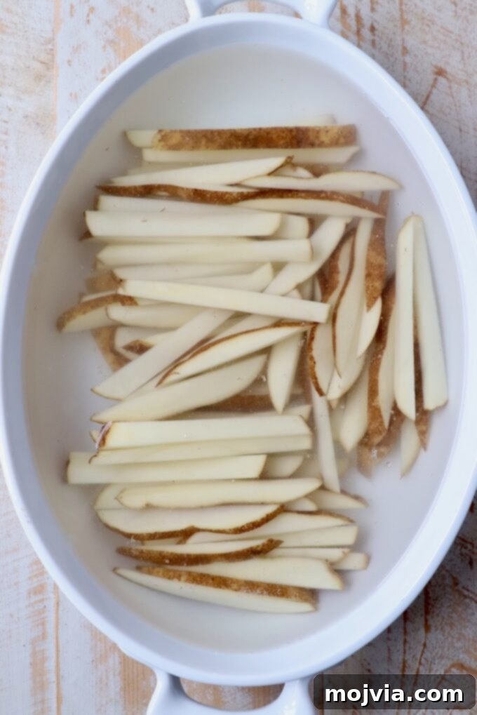Crispy Air Fryer Fries 5 Sliced potatoes soaking in a casserole dish filled with cold water, a crucial step for achieving extra crispy french fries.
