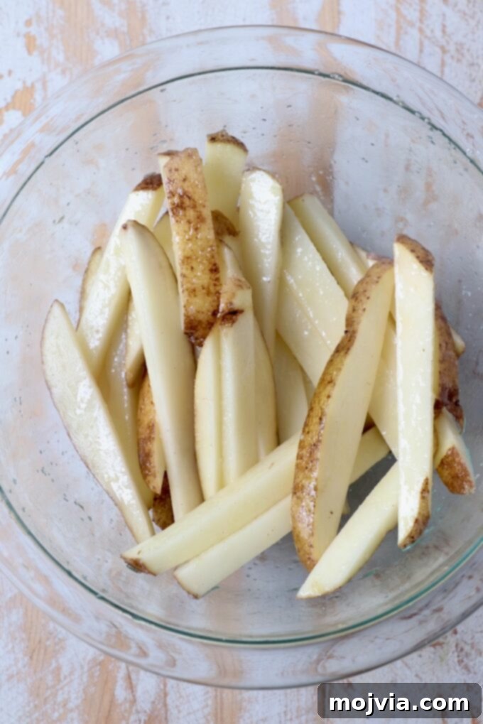 Crispy Air Fryer Fries 6 Uncooked, freshly sliced french fries resting in a clear glass bowl, ready for oiling and seasoning.