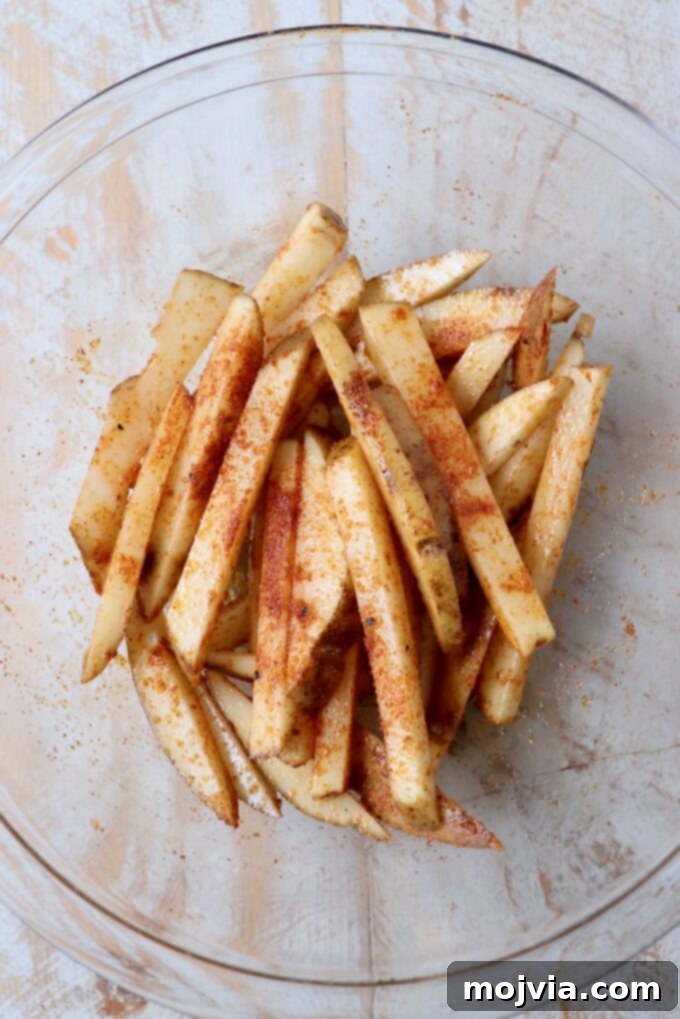Crispy Air Fryer Fries 7 Uncooked french fries in a glass bowl, now coated with olive oil and seasoned with a savory fry blend.