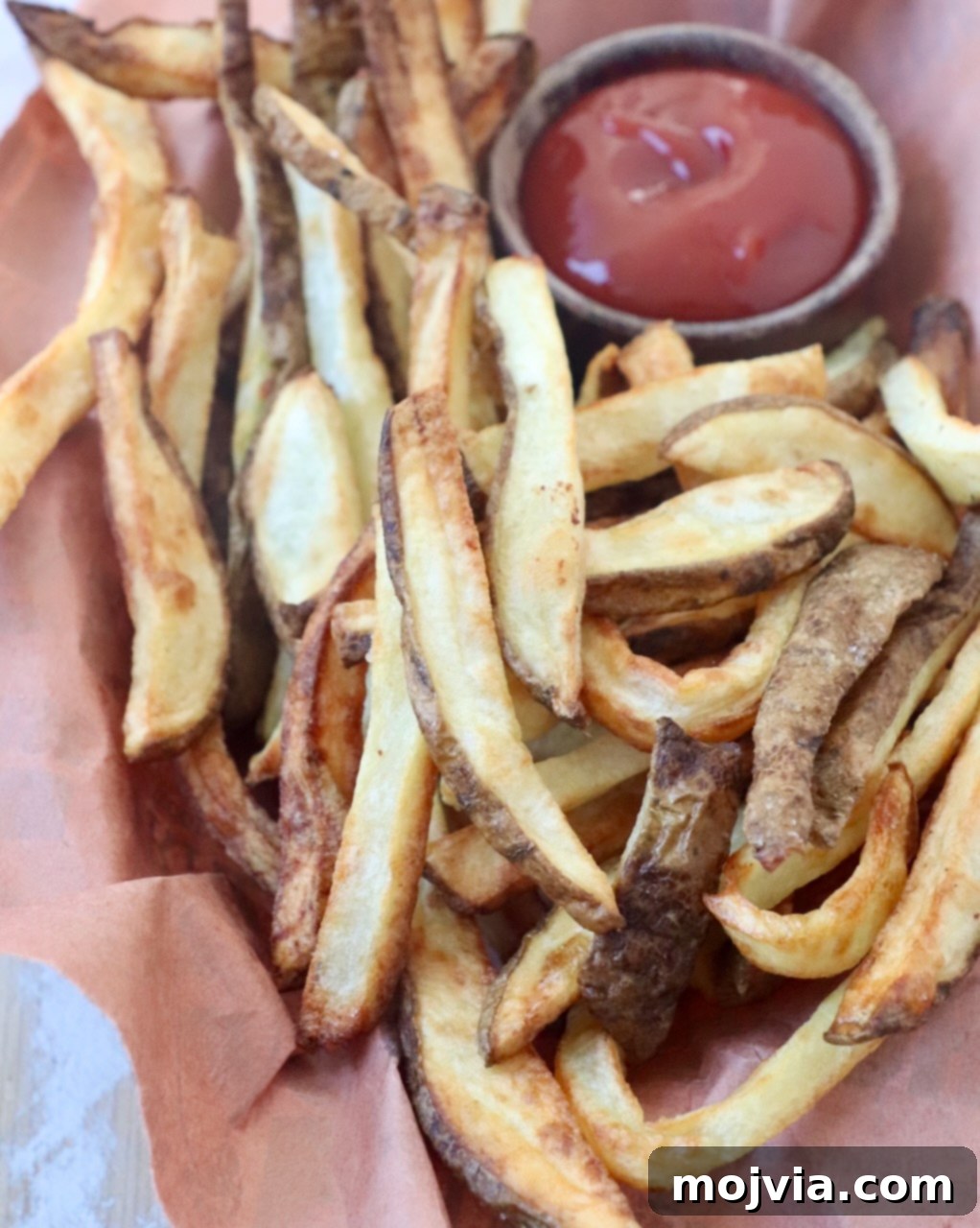 Crispy Air Fryer Fries 10 A basket full of cooked, golden-brown air fryer french fries, accompanied by a small bowl of ketchup for dipping.