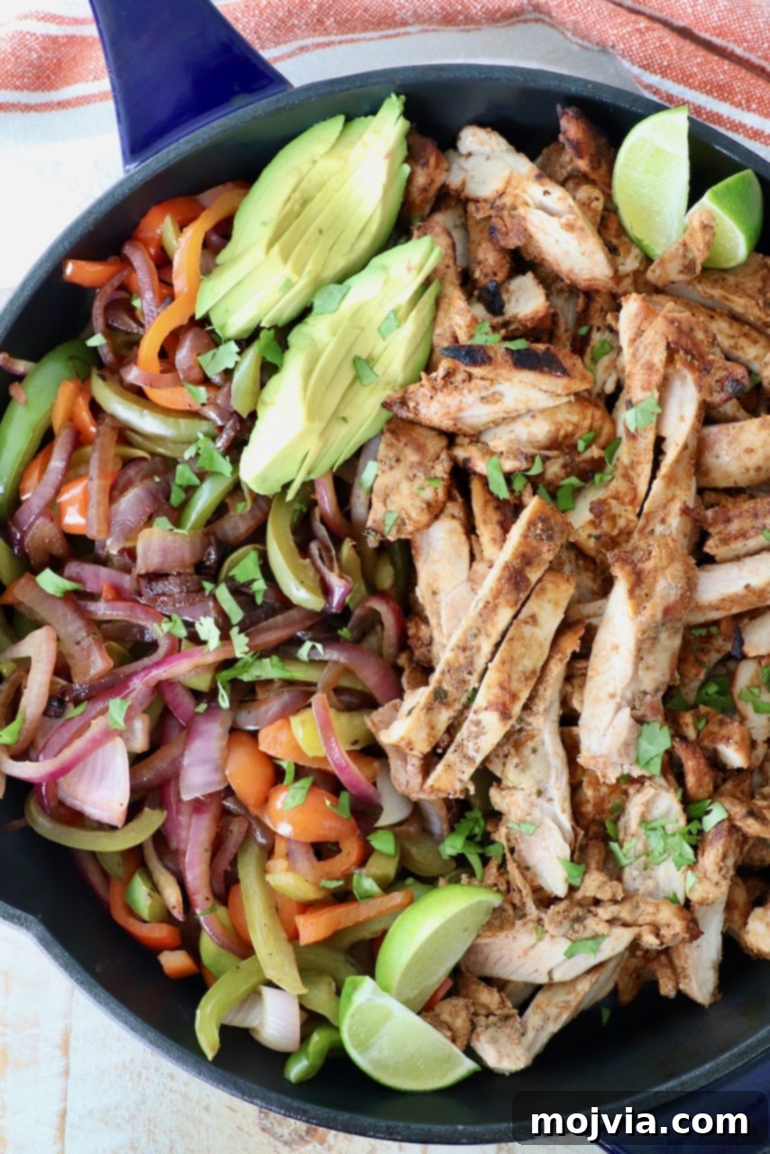 Grilled chicken and colorful vegetables sizzling in a cast iron skillet, garnished with sliced avocado and lime wedges