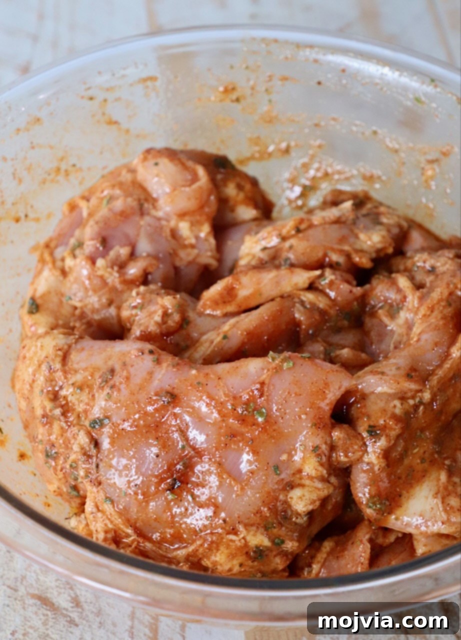 Raw chicken thighs coated in a rich, flavorful marinade in a large glass bowl, ready for marination