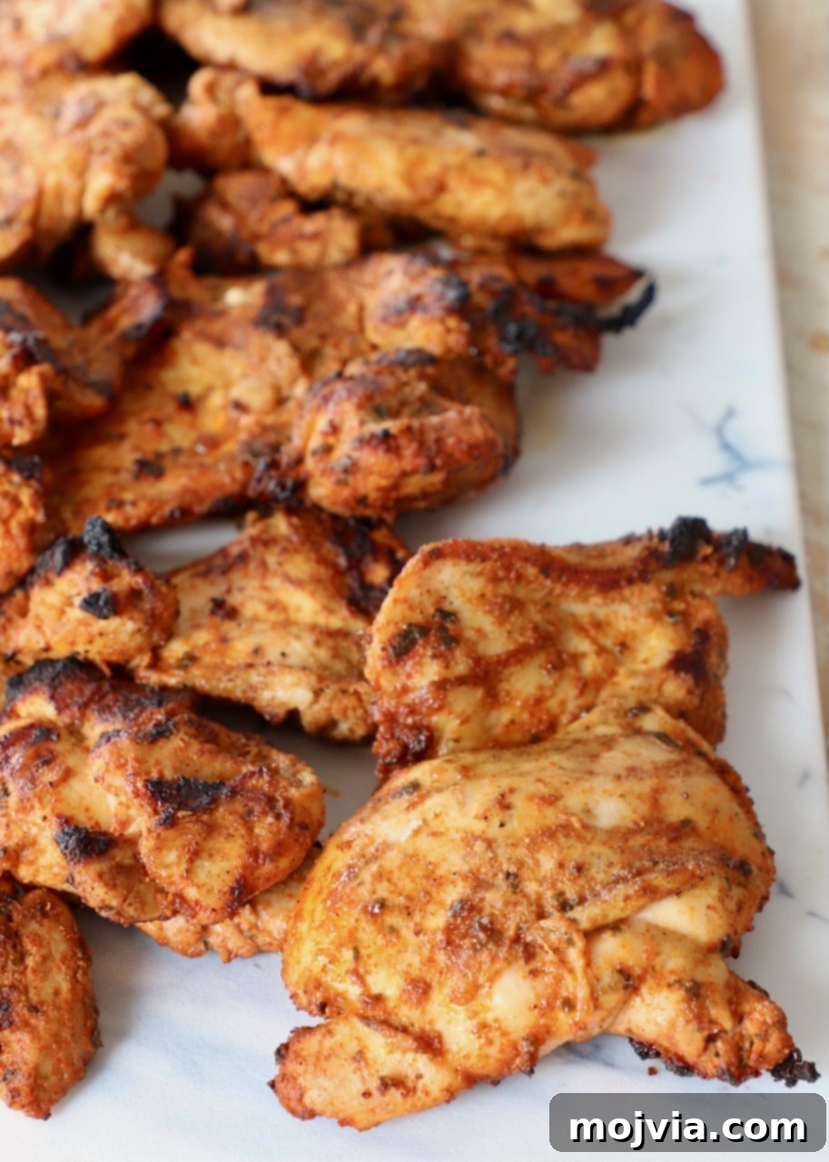 Perfectly grilled chicken thighs, golden brown and juicy, resting on a white cutting board after cooking