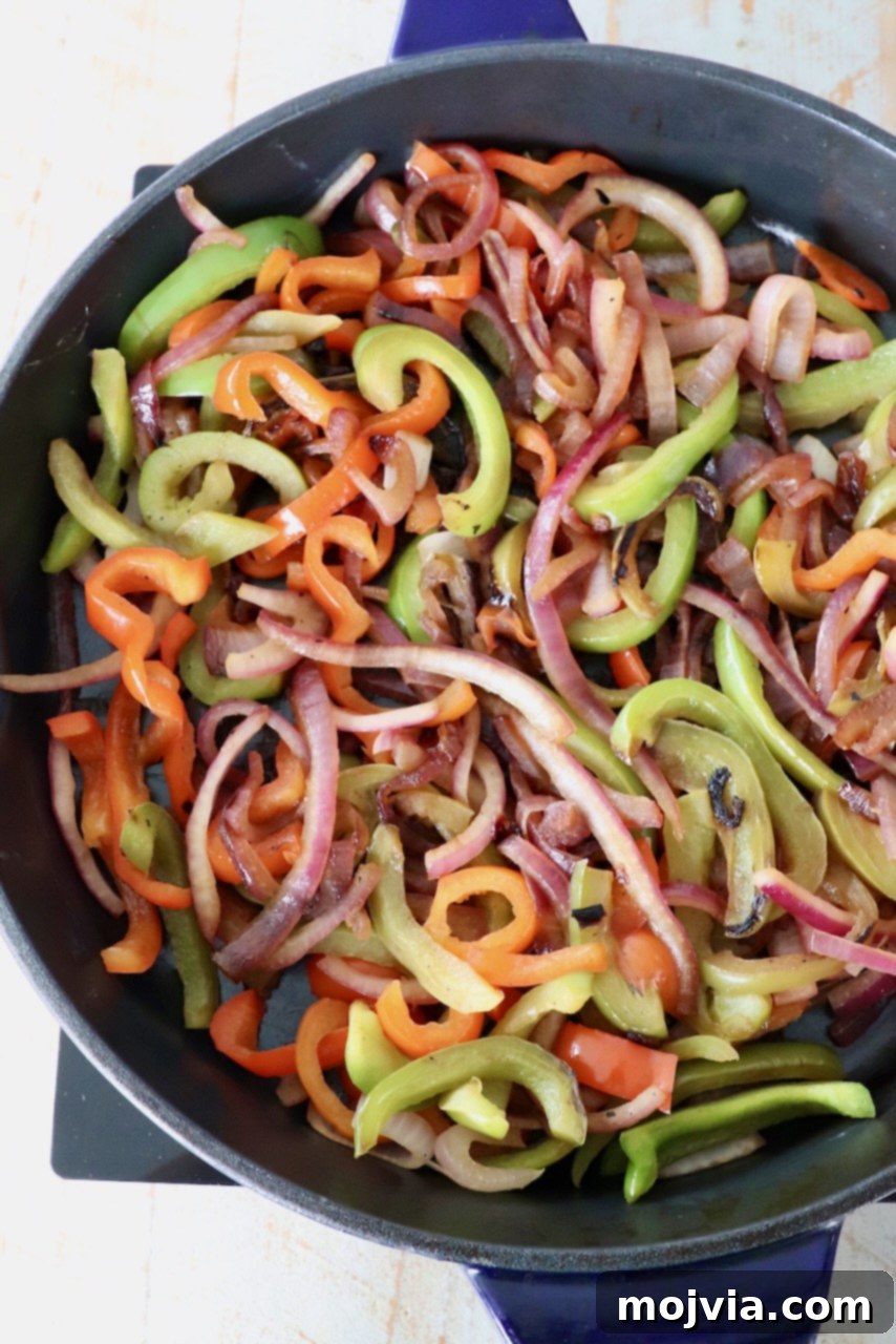 Cooked, tender-crisp sliced bell peppers and onions in a large cast iron skillet, perfectly caramelized