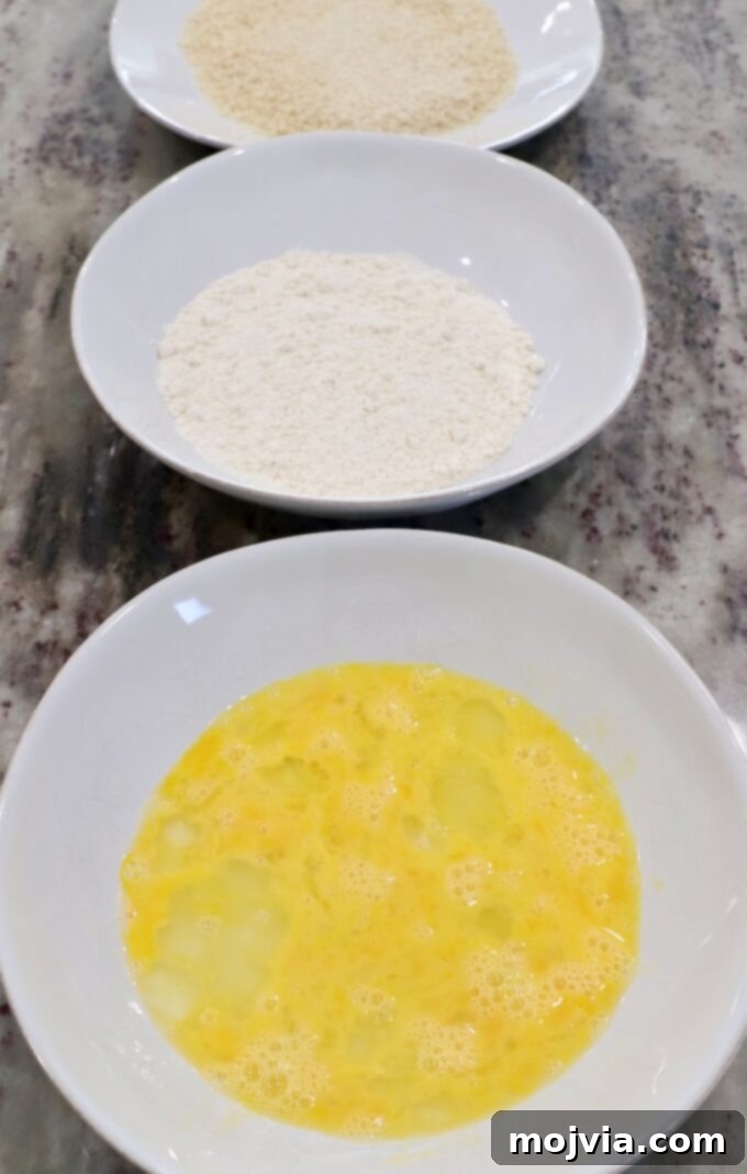 Crispy Boneless Bites 4 three bowls on countertop, one with whisked egg, one with flour and one with breadcrumbs