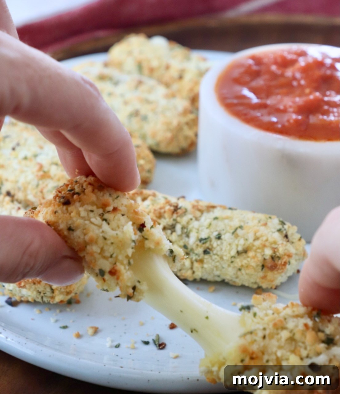 Crispy Air-Fried Mozzarella Sticks 2 A delicious air-fried mozzarella stick being pulled in half, showing the stretchy, melted cheese inside against a dark background.