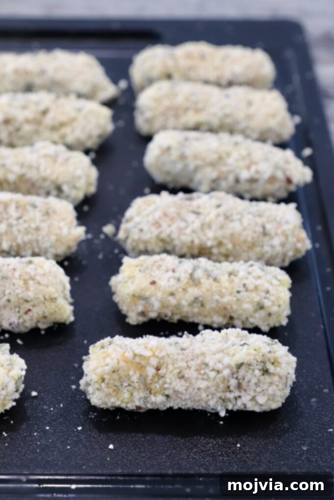 Crispy Air-Fried Mozzarella Sticks 7 Several perfectly breaded mozzarella sticks lined up on a wooden cutting board, ready for freezing.