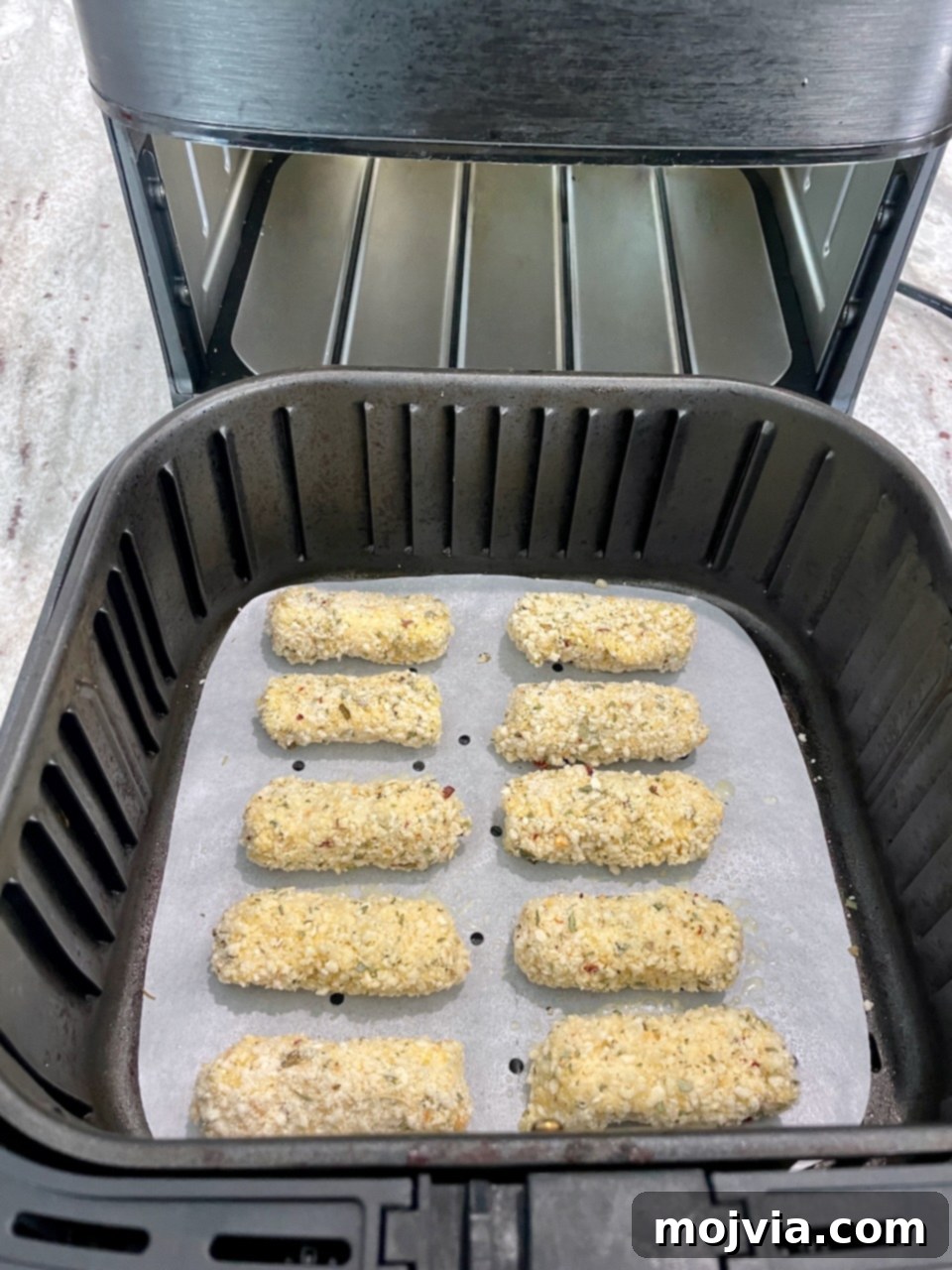 Crispy Air-Fried Mozzarella Sticks 8 Crispy breaded mozzarella sticks arranged in a single layer inside an air fryer basket, ready to be cooked.