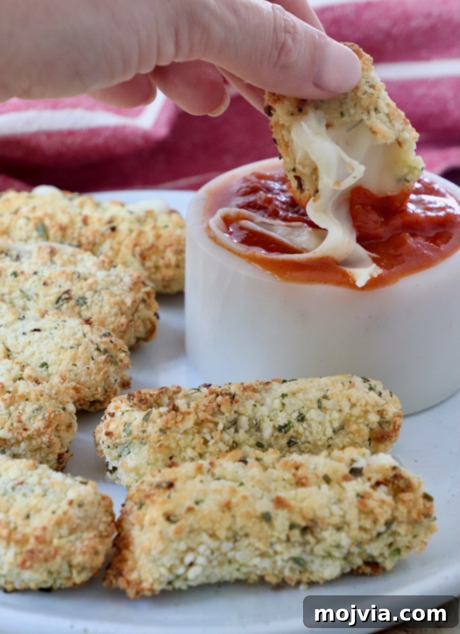 Crispy Air-Fried Mozzarella Sticks 9 Golden brown air fryer mozzarella sticks on a plate, with one being dipped into a small bowl of rich red marinara sauce.