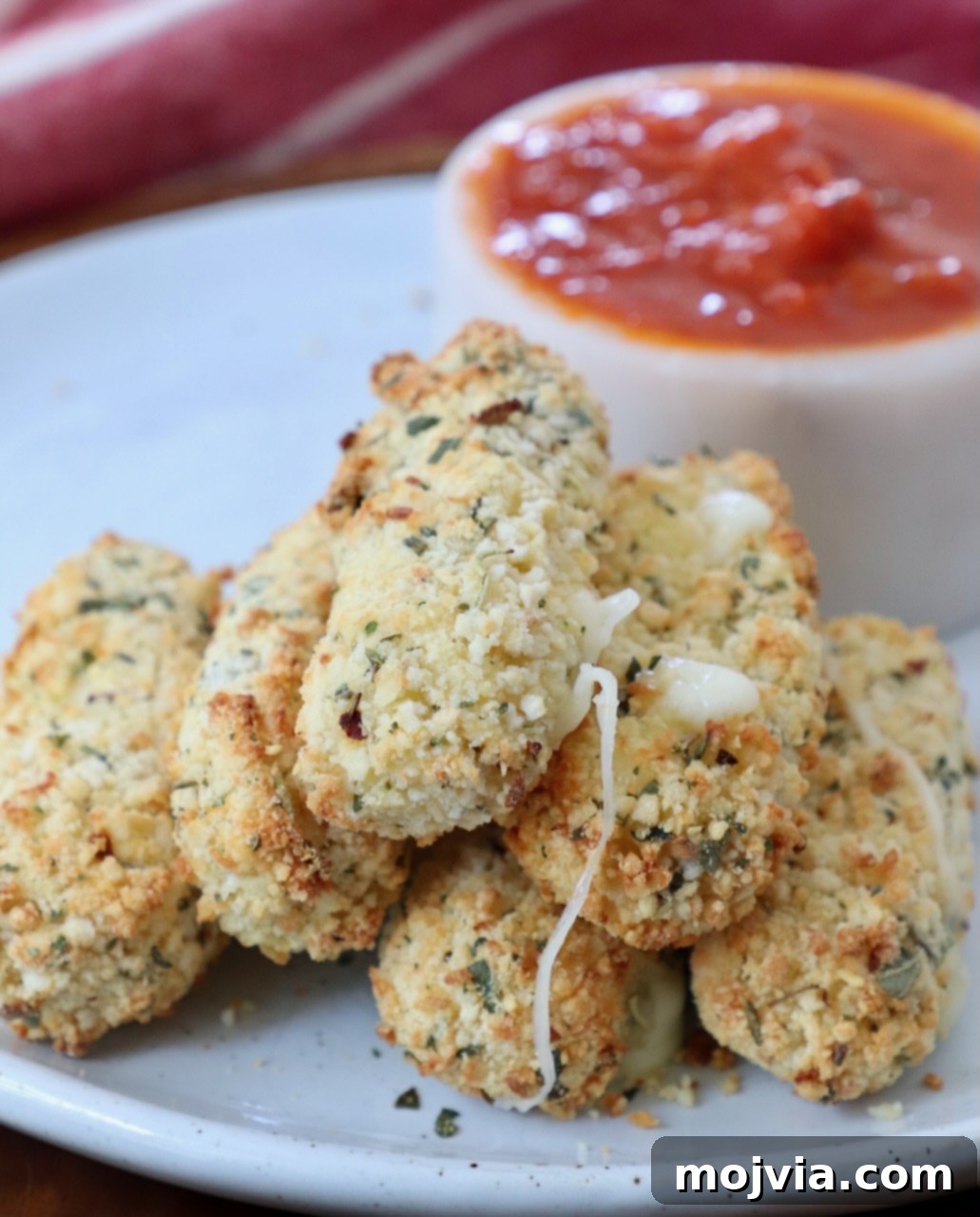 Crispy Air-Fried Mozzarella Sticks 10 A stack of perfectly cooked, golden-brown mozzarella sticks on a white plate, ready to be served alongside a small bowl of marinara sauce.