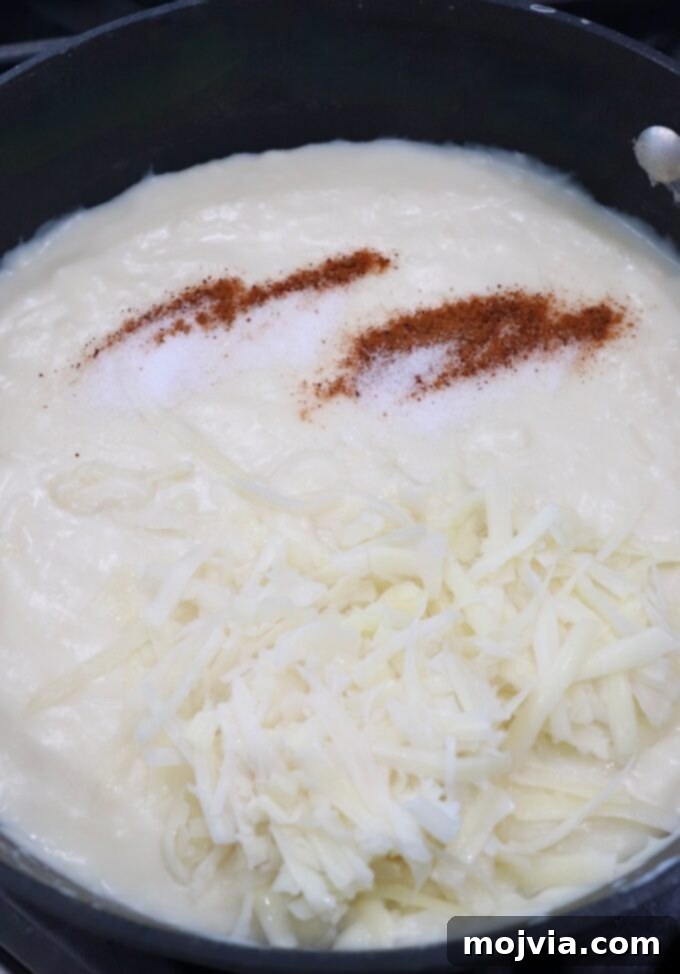 Creamy Greek Comfort Bake 11 Thickened béchamel sauce in a skillet, seasoned with nutmeg and salt, and mixed with shredded Kefalotyri cheese.