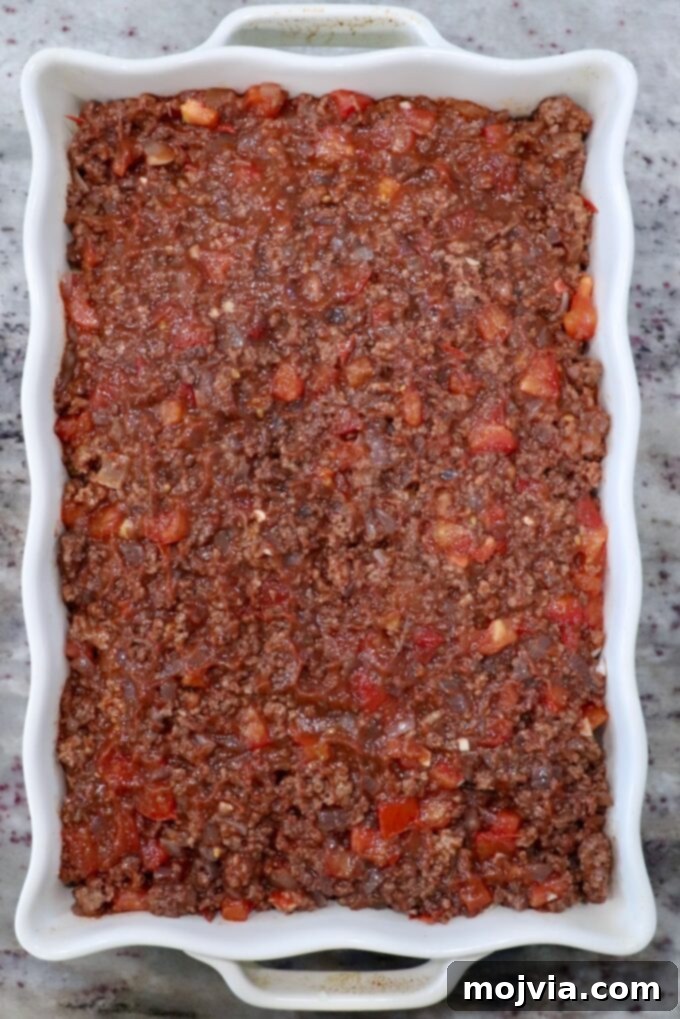 Creamy Greek Comfort Bake 12 The cooled, rich tomato meat sauce evenly spread over the pasta layer in a casserole dish, forming the second layer of Pastitsio.
