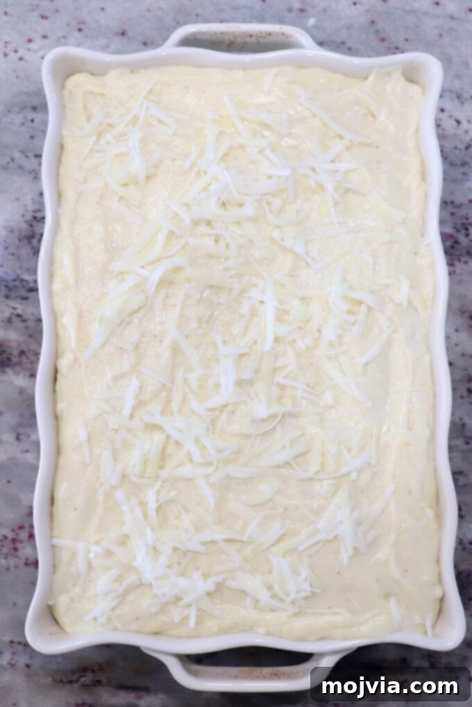 Creamy Greek Comfort Bake 14 The fully assembled, uncooked Pastitsio in a casserole dish, topped with béchamel and ready for the oven, showing distinct layers.