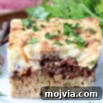 A delicious slice of cooked Pastitsio on a white plate, ready to be enjoyed.