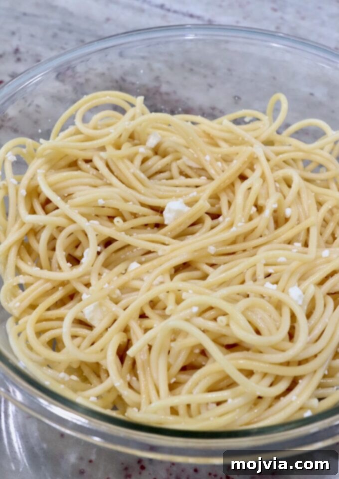 Creamy Greek Comfort Bake 4 Cooked Pastitsio pasta noodles in a large bowl with crumbled feta cheese ready to be mixed.
