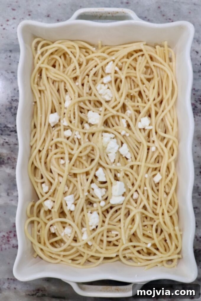 Creamy Greek Comfort Bake 5 Cooked Pastitsio pasta noodles expertly arranged lengthwise in a large casserole dish, topped with feta cheese crumbles.