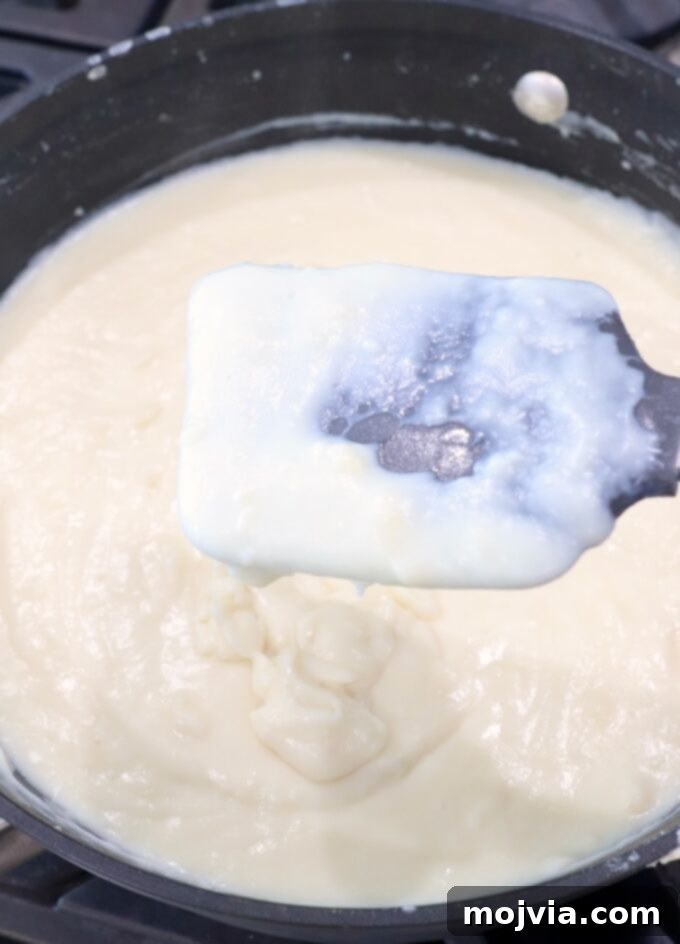 Creamy Greek Comfort Bake 10 A rich, creamy béchamel sauce, perfectly thickened and smooth, in a skillet with a rubber spatula.