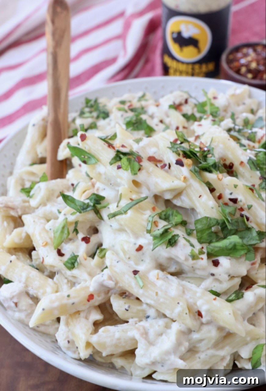 cooked penne pasta tossed with chicken and sauce in bowl with spoon, garnished with fresh herbs