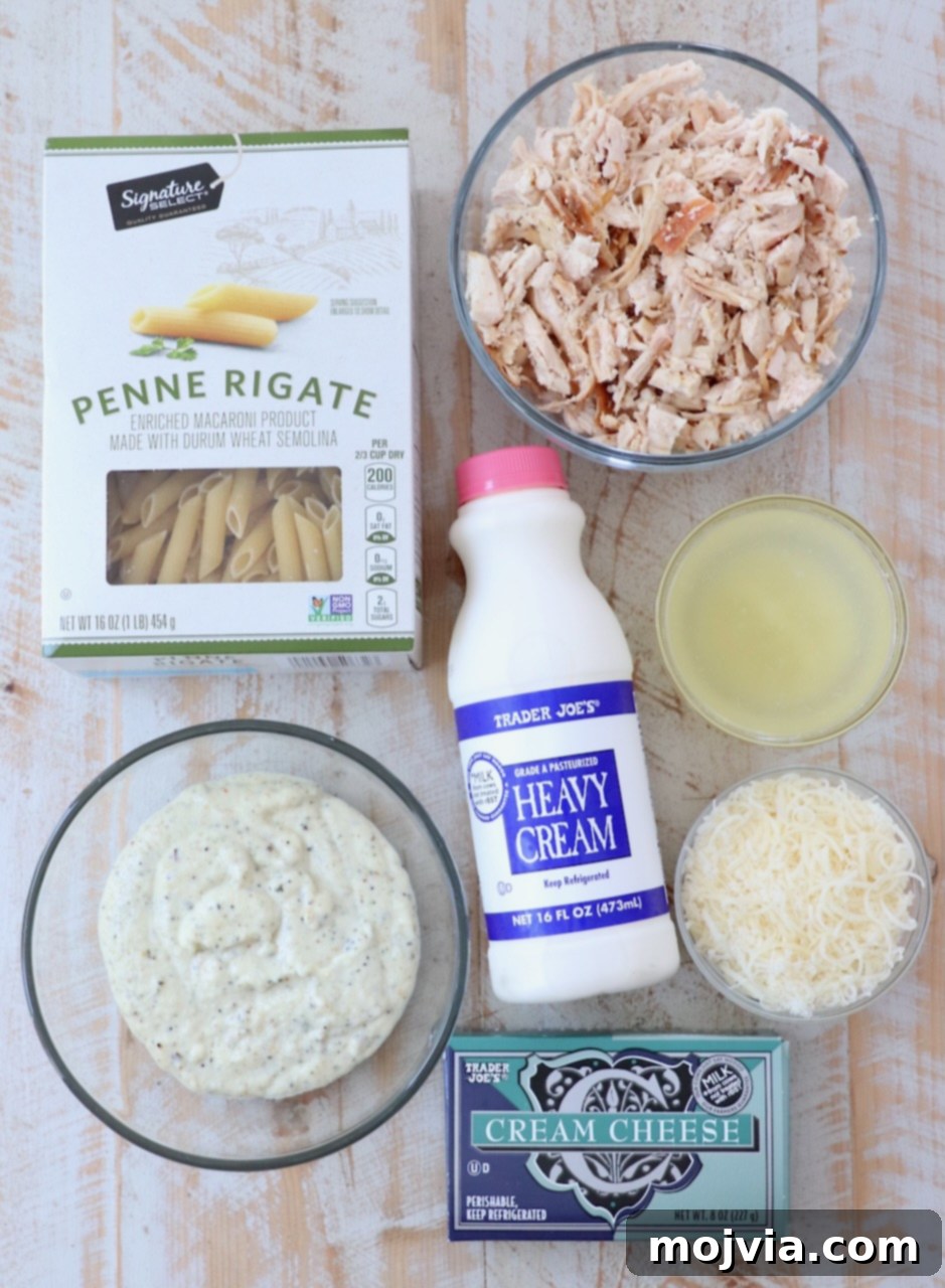 ingredients for garlic parmesan chicken pasta on white wood board, including chicken, cheese, pasta, and sauces