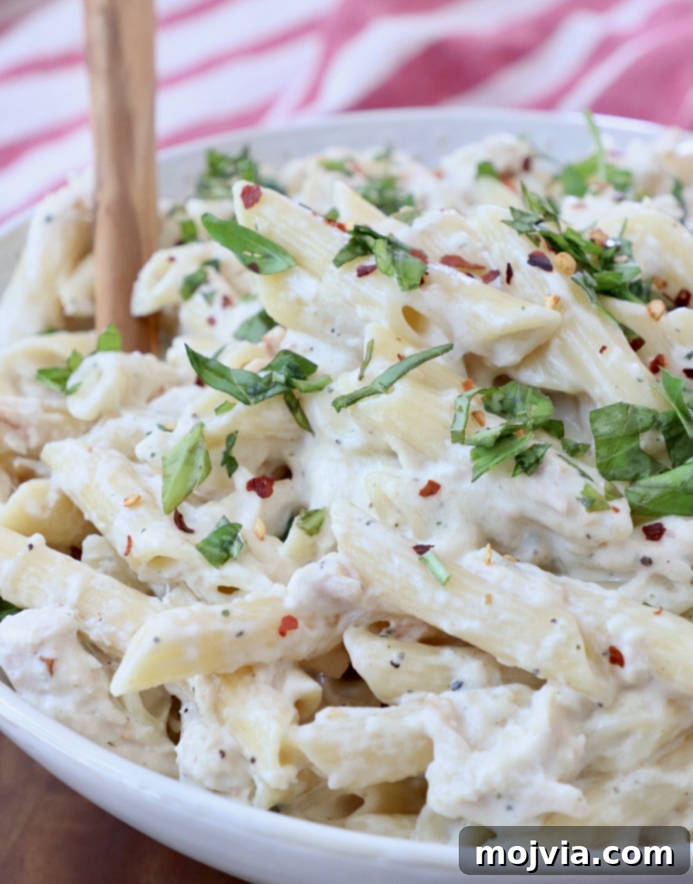 pasta tossed with creamy sauce in bowl with serving spoon, ready to be dished out