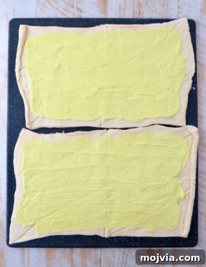 mayonnaise and mustard combined and spread on sheets of crescent roll dough on a large cutting board