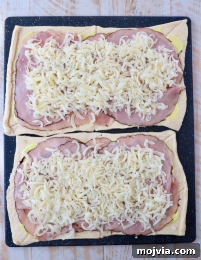 crescent roll dough sheets topped with sliced ham and shredded swiss cheese