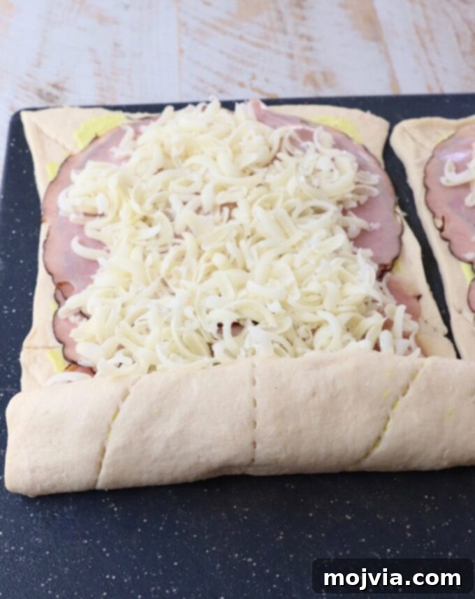 crescent roll dough rolled up over ham and swiss cheese on a cutting board