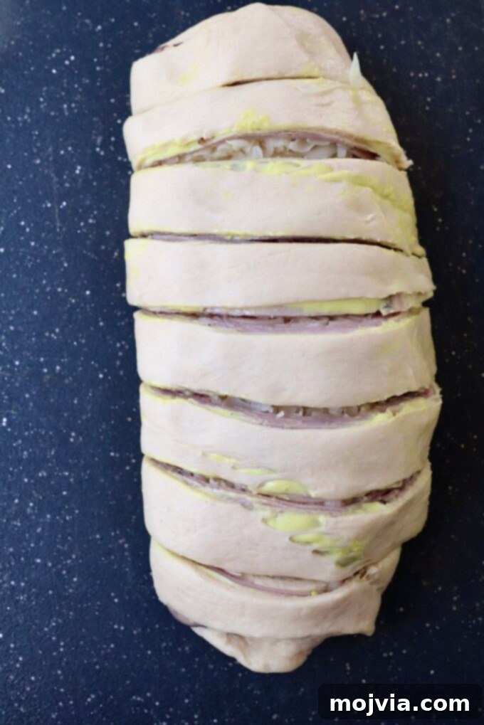 crescent roll dough rolled up over ham and swiss, sliced in one inch sections on a cutting board