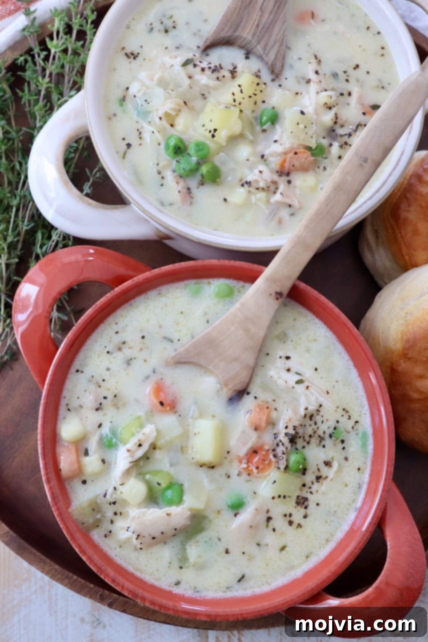 Cozy Chicken Pot Pie Soup 12 Two white bowls brimming with creamy Chicken Pot Pie Soup, garnished with fresh herbs and served with spoons, ready for a comforting meal.