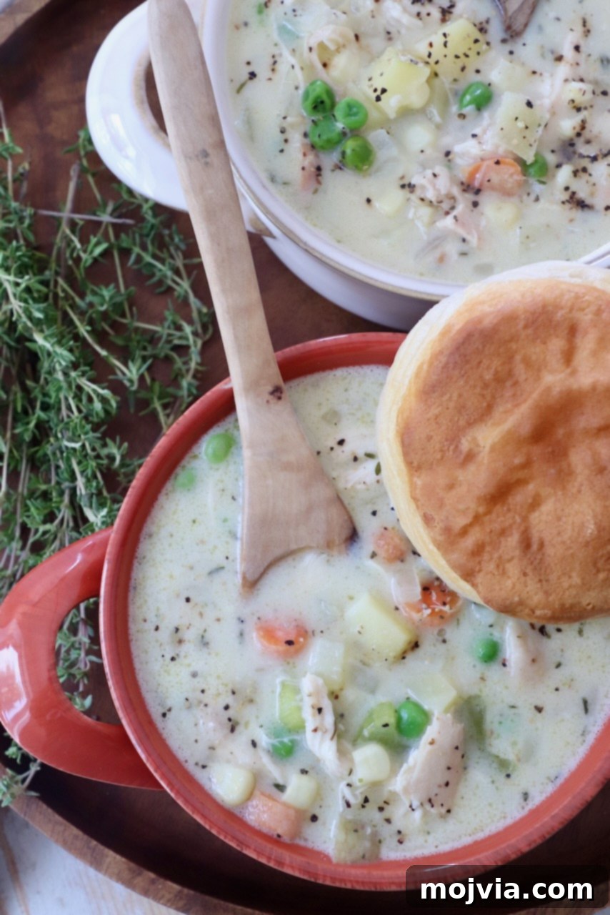 Cozy Chicken Pot Pie Soup 13 A warm bowl of creamy Chicken Pot Pie Soup, garnished with fresh thyme and topped with a fluffy golden-brown biscuit for dipping, on a rustic wooden surface.