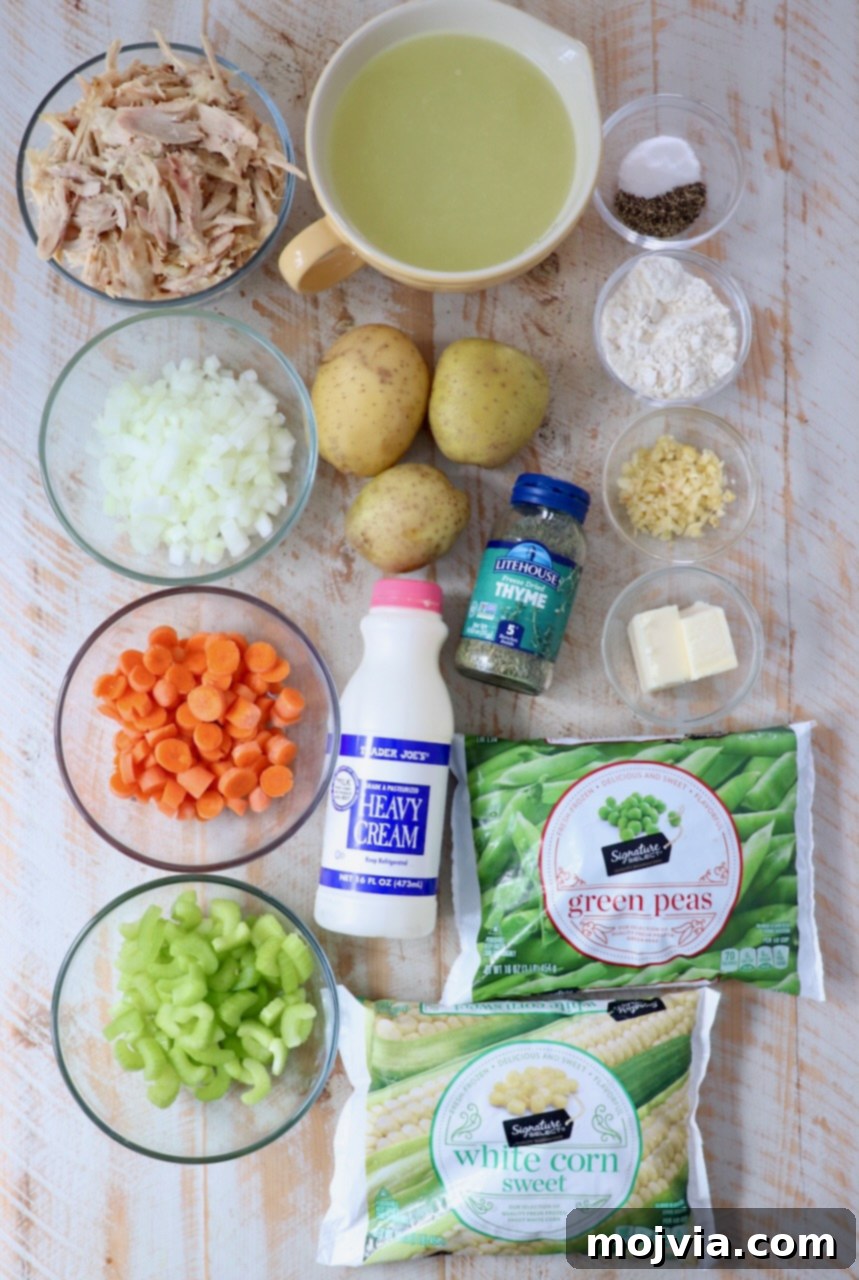 Cozy Chicken Pot Pie Soup 3 An array of fresh ingredients for Chicken Pot Pie Soup, including diced carrots, celery, onions, garlic, potatoes, chicken broth, and herbs, arranged on a rustic white wooden board.