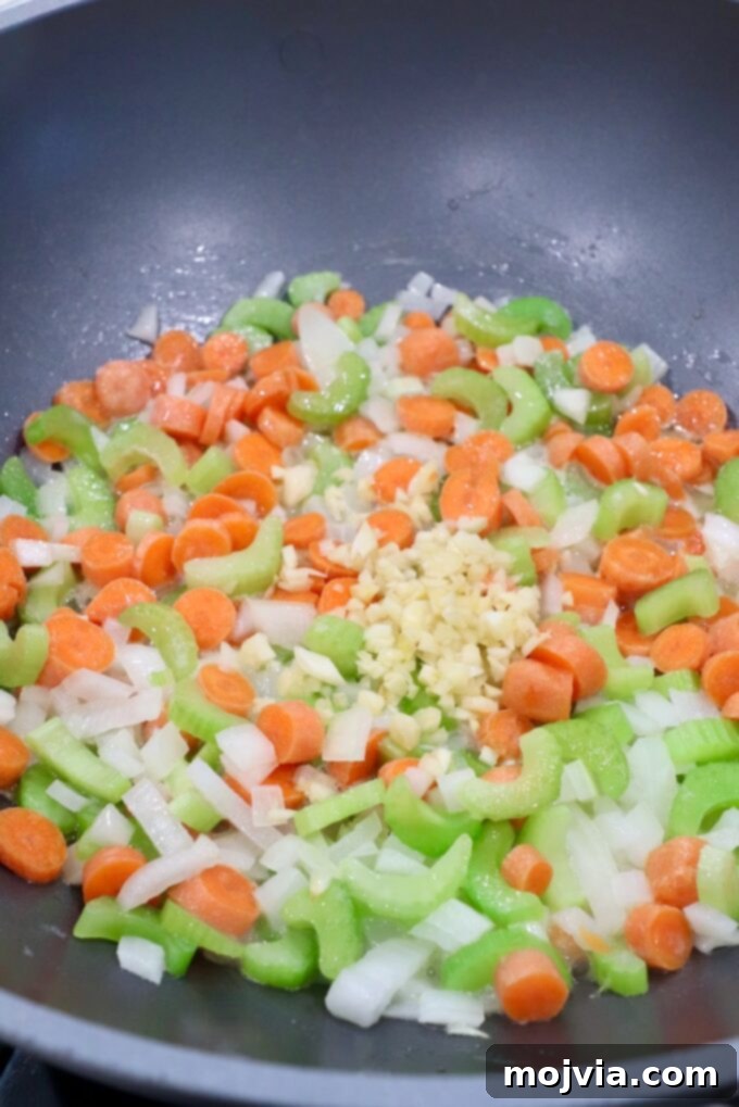 Cozy Chicken Pot Pie Soup 4 Diced carrots, onions, celery, and minced garlic simmering in melted butter in a large skillet, forming the aromatic base for the soup.