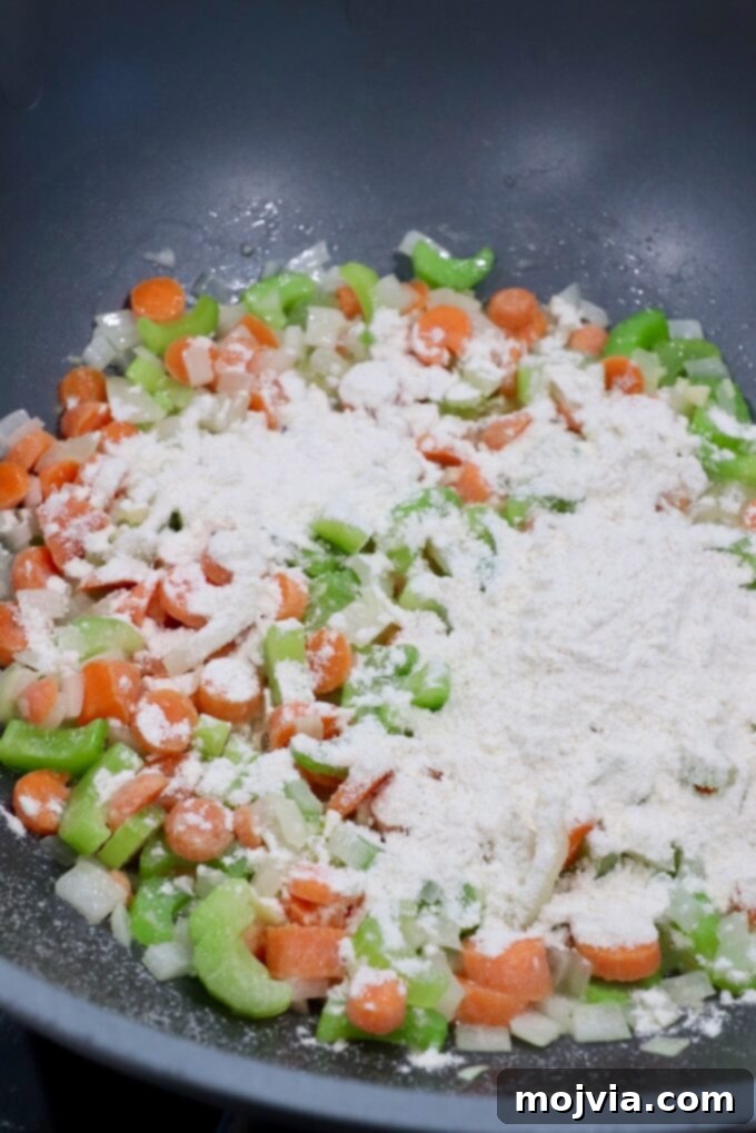Cozy Chicken Pot Pie Soup 5 All-purpose flour sprinkled evenly over softened diced vegetables in a skillet, ready to be stirred to create a roux and thicken the soup.