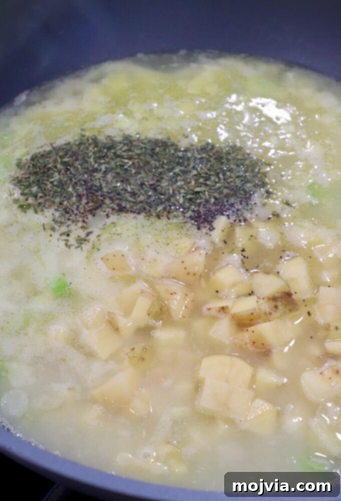 Cozy Chicken Pot Pie Soup 8 Diced Yukon gold potatoes, dried thyme, salt, and black pepper added to boiling chicken broth and vegetables in a skillet, ready to simmer.