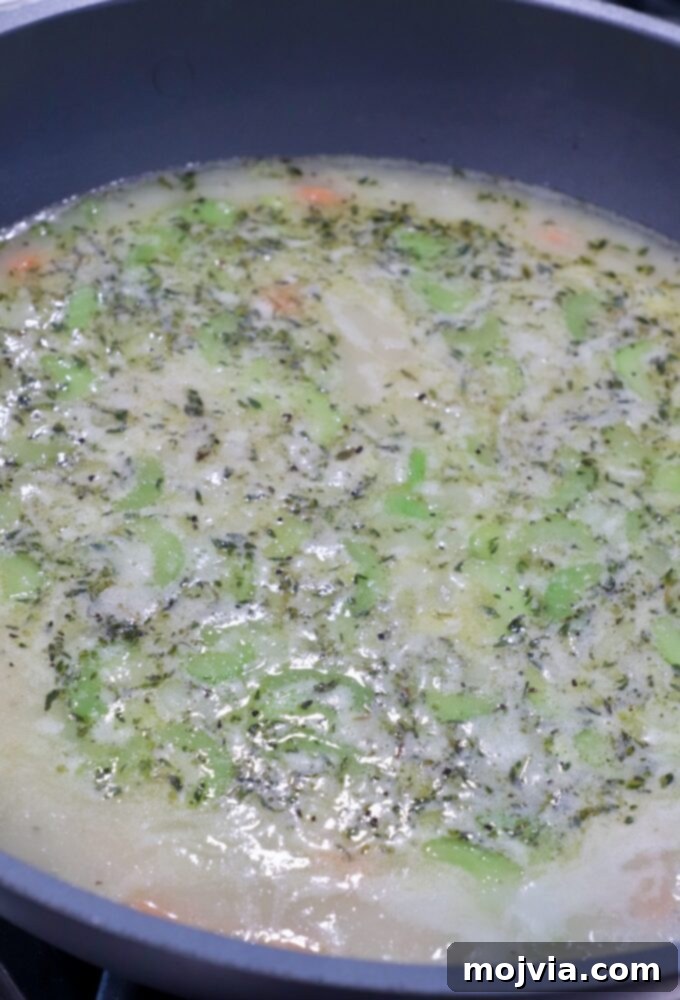 Cozy Chicken Pot Pie Soup 9 A simmering pot of seasoned chicken broth and diced vegetables, including carrots, celery, onions, and potatoes, forming a hearty soup base.
