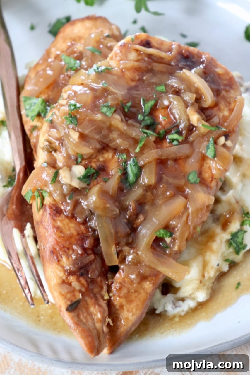 Rich Slow Cooker French Onion Chicken 2 Cooked French Onion Chicken breasts on a plate with caramelized onion gravy and mashed potatoes.